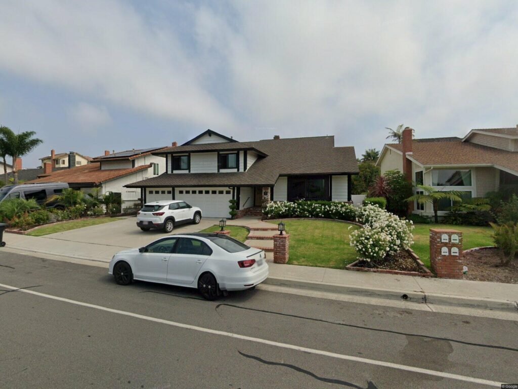 California real estate house with lawn, driveway, parked cars, and neighboring homes